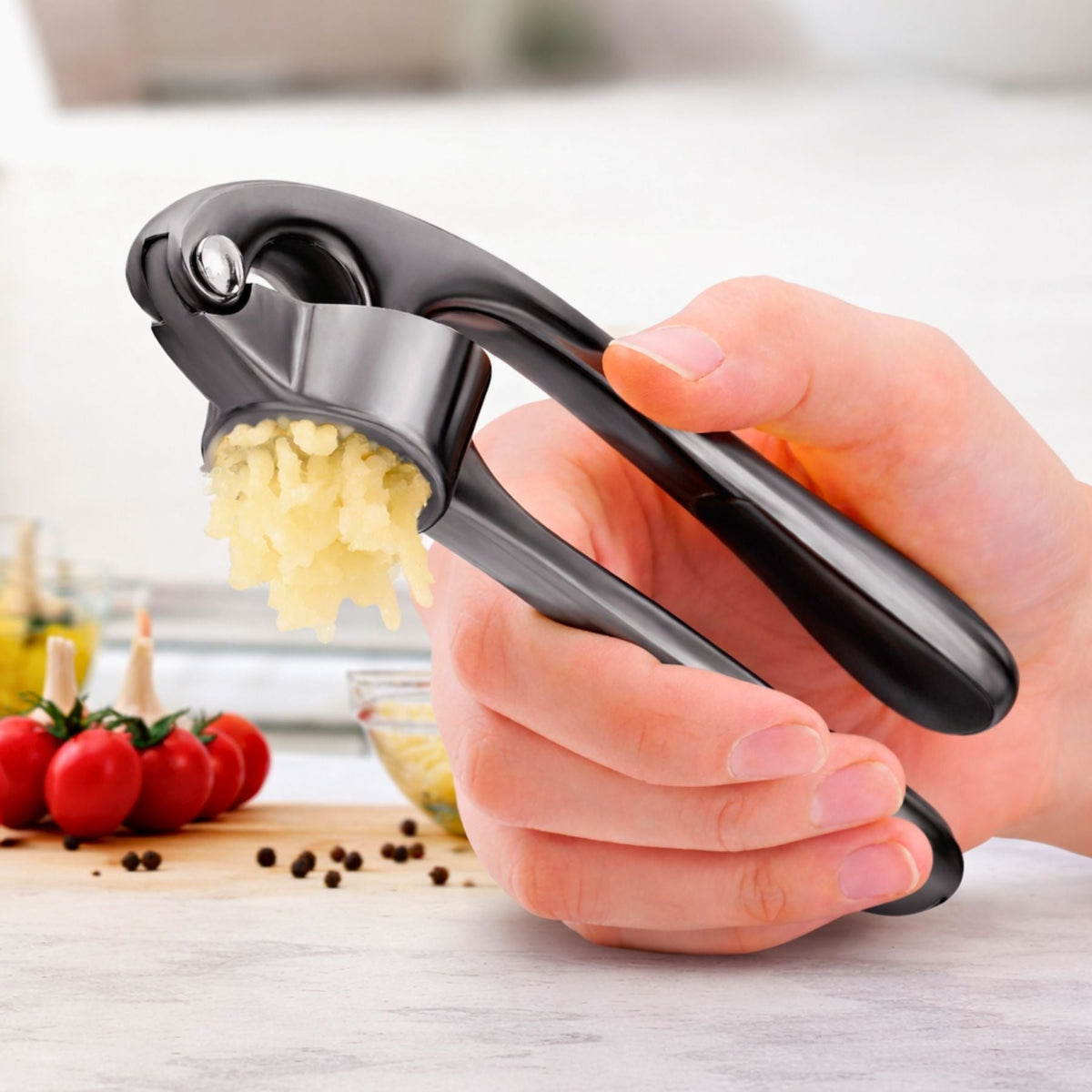Hand using a Zuki Garlic Press Set with crushed garlic on a kitchen counter.